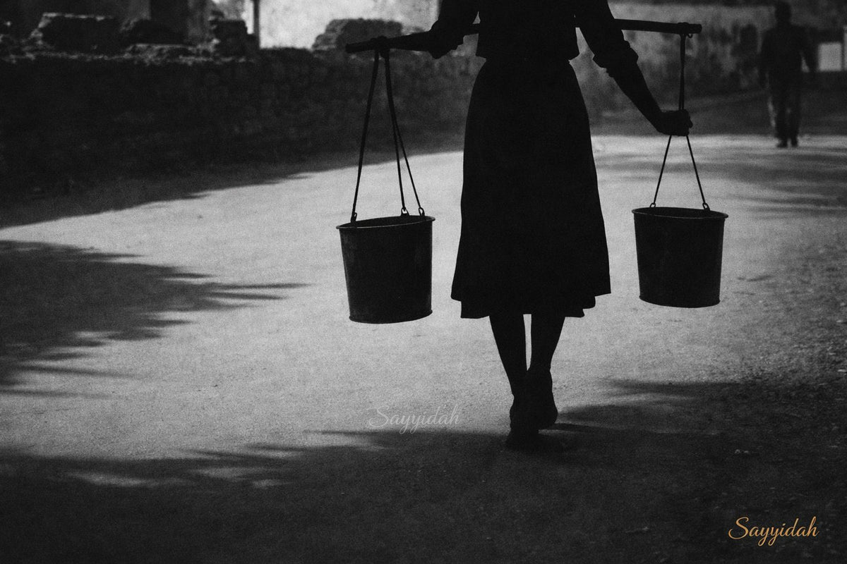 Black and white silhouette of a person carrying water buckets with strong shadow contrast in a cultural fine art style